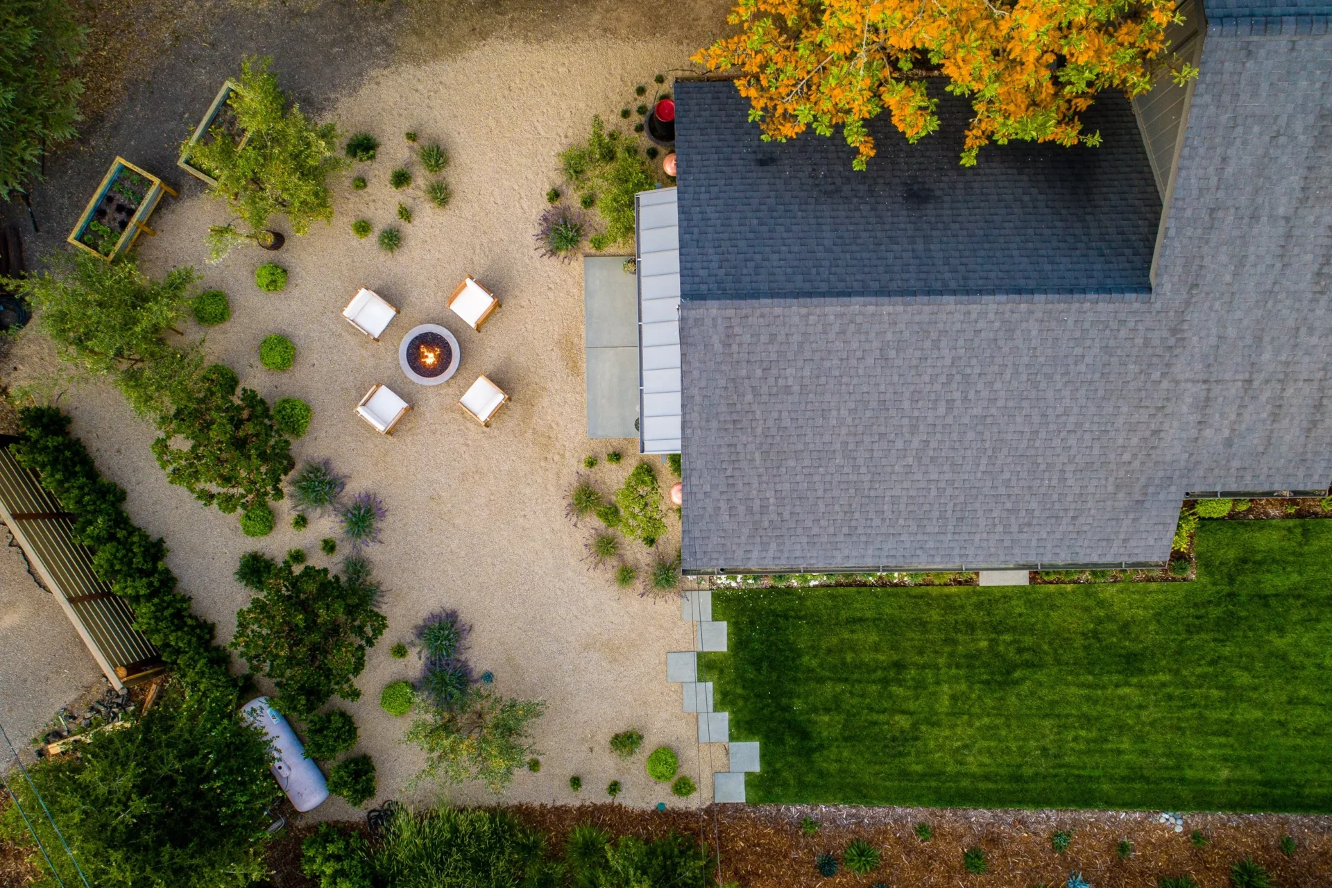 Aerial View | AAA Landscaping Aerial view of a beautifully landscaped backyard featuring a fire pit seating area, gravel pathways, lush greenery, and a well-maintained lawn.